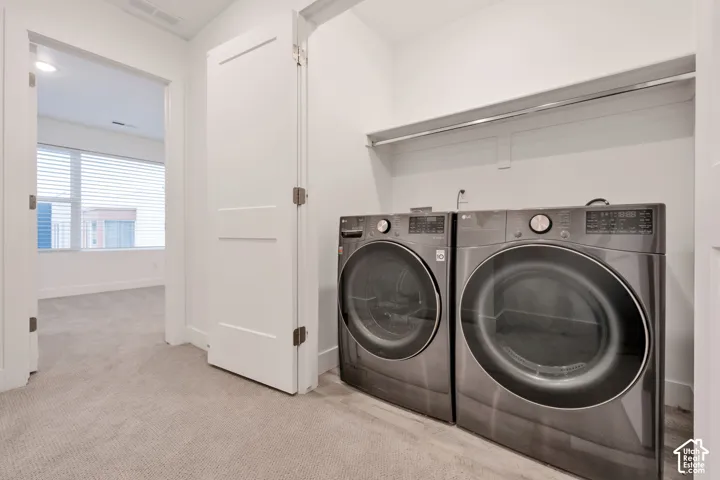 Laundry closet featuring high-efficiency front-load appliances, built-in shelving, and carpeting