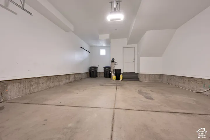 Finished garage with concrete flooring, smooth wall finishes, overhead lighting, and an access door with stairs