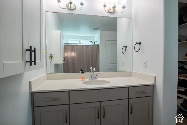 Bathroom vanity featuring grey shaker-style cabinetry, a light-toned solid surface countertop with an integrated oval sink, a large frameless mirror, and brushed-finish hardware