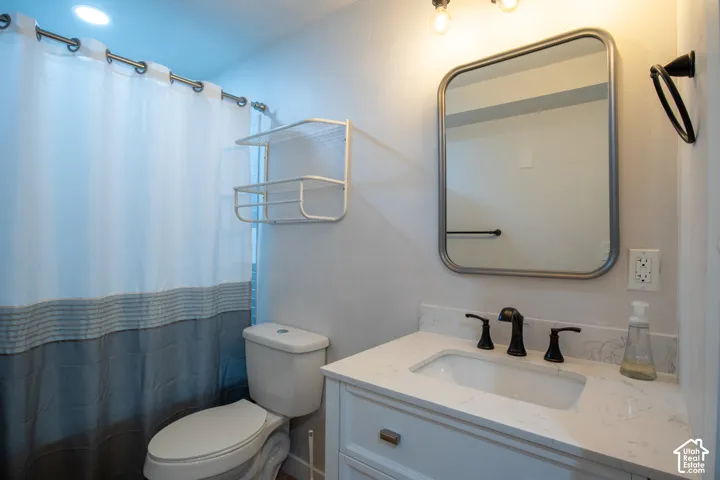 Vanity featuring a stone-composite countertop with an integrated rectangular sink and oil-rubbed bronze widespread faucet, accompanied by a rectangular wall-mounted mirror, three-light overhead fixture, and white cabinetry