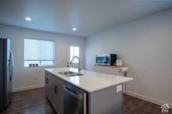 Kitchen featuring an island with a dual-basin sink and stone-finish countertop, stainless steel dishwasher, grey shaker-style cabinetry, and wood-finish flooring