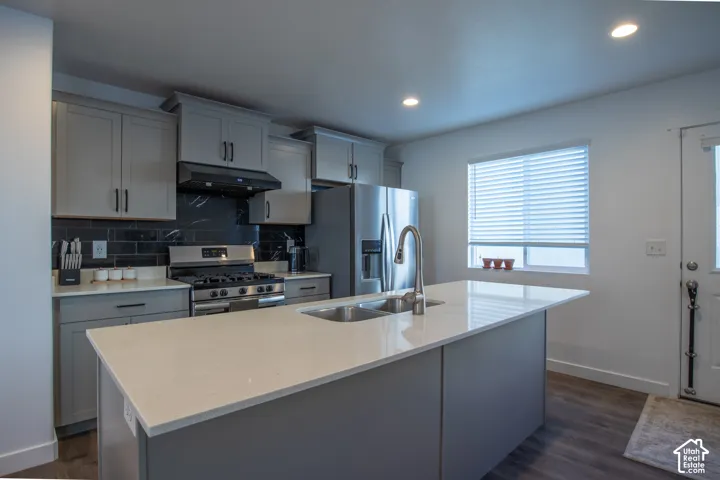 Kitchen featuring shaker-style cabinetry, a central island with a solid surface countertop, stainless steel appliances, a dark tile backsplash, and wood-finish flooring