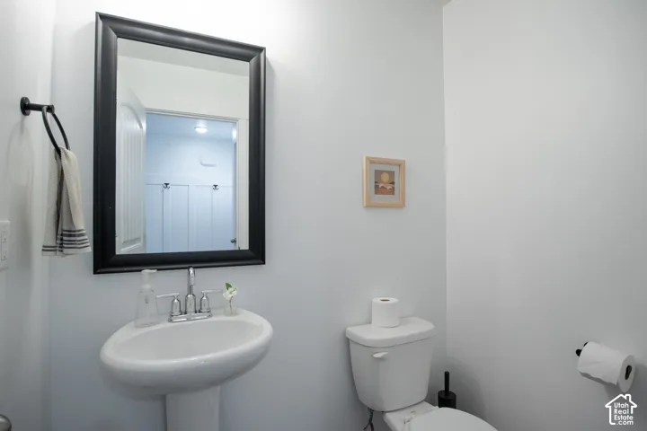 Powder room featuring a white pedestal sink, chrome widespread faucet, black-framed wall mirror, and toilet with a coordinating black toilet paper holder and towel ring