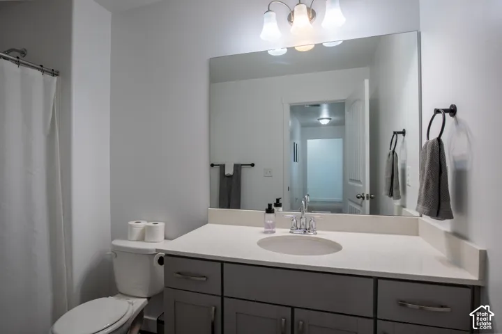 Shaker-style grey vanity, integrated stone-composite countertop with an oval under-mount sink, polished chrome faucet, full-width vanity mirror, and three-light decorative vanity fixture