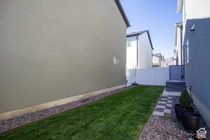 Side yard featuring a grass lawn, decorative stone borders, stone paver pathway, and a white vinyl privacy fence
