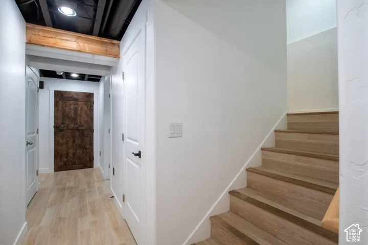 Interior hall featuring wood-finish flooring, a rustic wood-plank door, exposed structural beam, and wood-finish staircase treads