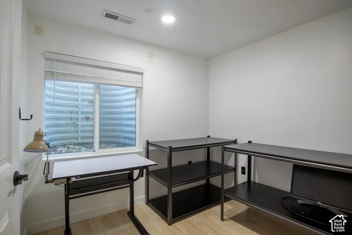 Neutral-toned interior space featuring wood-finish flooring, a recessed window with an integrated window well, and overhead recessed lighting
