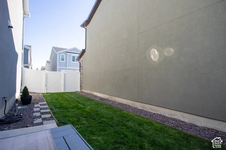 Side yard featuring a stucco exterior finish, white vinyl privacy fencing, manicured grass, and decorative stone landscaping
