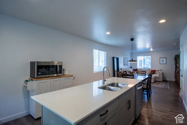 Kitchen island featuring white countertops, a stainless-steel dual-basin sink, and gray shaker-style cabinetry with matte black hardware, complemented by wood-finish flooring and recessed lighting