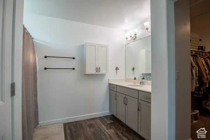 Bathroom featuring a single vanity with gray cabinetry, solid surface countertop, wall-mounted white cabinetry, wood-finish flooring, and a multi-bulb vanity light fixture