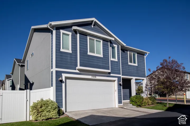 Two-story exterior featuring blue horizontal siding, a white double-car garage door, concrete driveway, and white vinyl privacy fencing