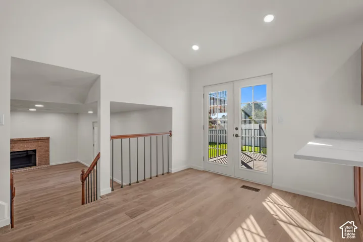 Vaulted ceilings, wood-finish flooring, glass-paned double doors, recessed lighting, and brick fireplace
