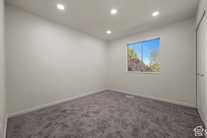 Neutral-toned interior room featuring grey carpeting, recessed lighting, a single-pane window, and double-door closet cabinetry