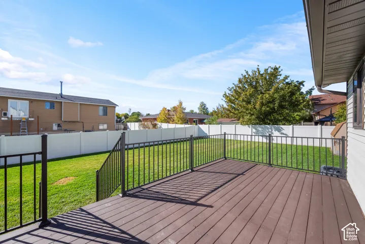 Elevated hard wood deck featuring black metal railing, stairs, and a fenced backyard with a lawn