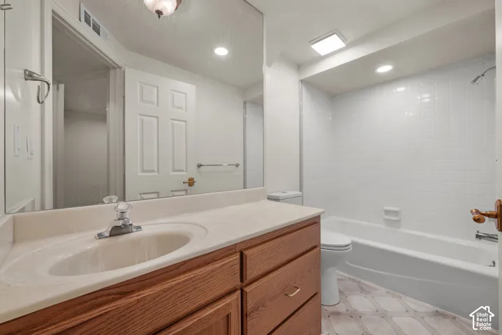 Bathroom featuring a wood-finish vanity with a molded countertop and sink, large wall-mounted mirror, white tile shower surround, and patterned flooring
