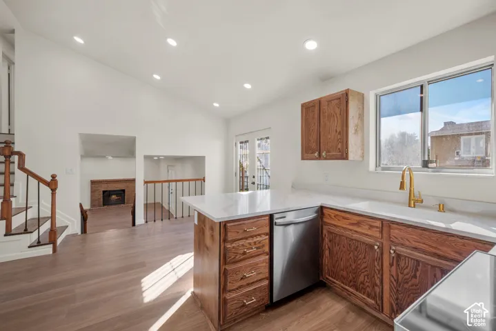 Kitchen featuring wood cabinetry, stone countertops, integrated stainless steel dishwasher, and gold-tone fixtures, complemented by wood-finish flooring and recessed lighting throughout the area