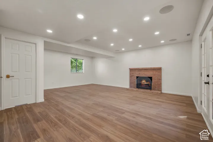 Open-concept interior featuring wood-finish flooring, brick fireplace surround, recessed lighting, surround sounds speakers, and glass-paneled double doors
