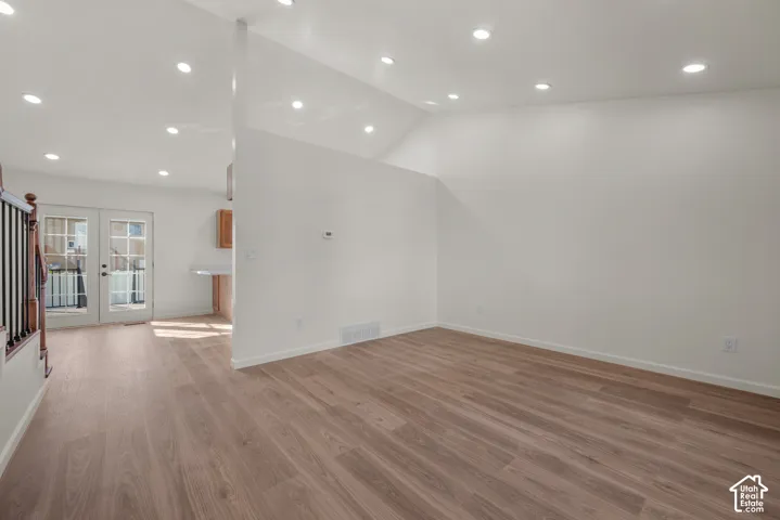 Open-concept interior featuring vaulted ceilings, wood-finish flooring, recessed lighting, and a multi-lite glass panel door