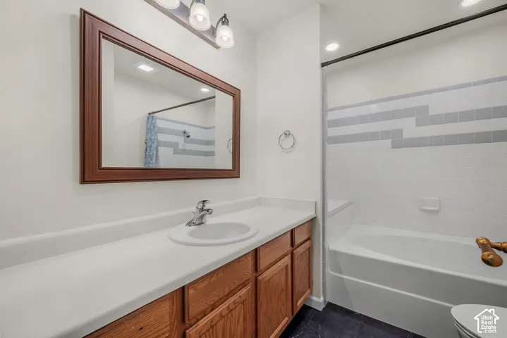 Bathroom featuring a wood-tone vanity, integrated solid-surface countertop with an oval basin, framed wall mirror, and a tub-shower combination with decorative tile detailing