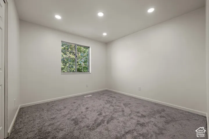 Neutral-toned room featuring grey wall-to-wall carpeting, recessed ceiling lighting, and a single-pane window with a view of mature trees