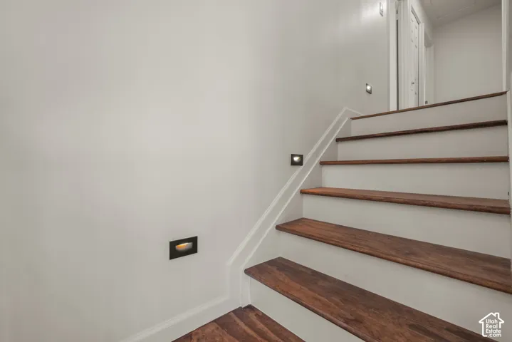 Staircase featuring wood-finish treads, painted risers, and recessed wall-mounted lighting