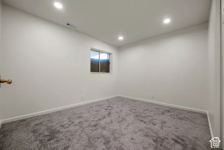 Neutral-toned wall paint, recessed lighting, carpeted flooring, and a sliding window