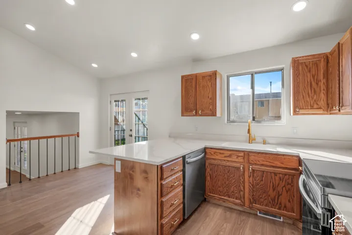 Kitchen featuring wood cabinetry, stone-finish countertops, stainless steel dishwasher, gold-toned faucet, and wood-finish flooring