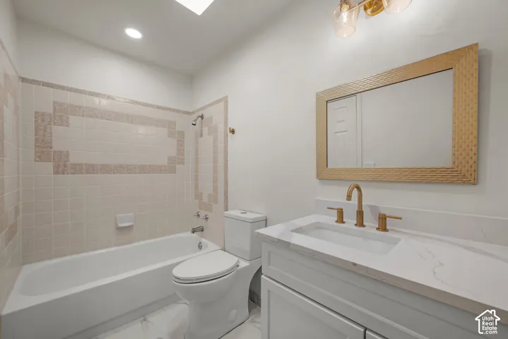 Bathroom featuring a white vanity with a stone countertop, an integrated rectangular sink, brass-finish hardware, and a tile-surround shower and bathtub combination