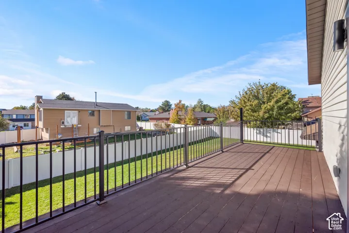 Elevated balcony deck featuring hard wood decking, black metal railing, and wall-mounted exterior lighting, overlooking a fenced backyard