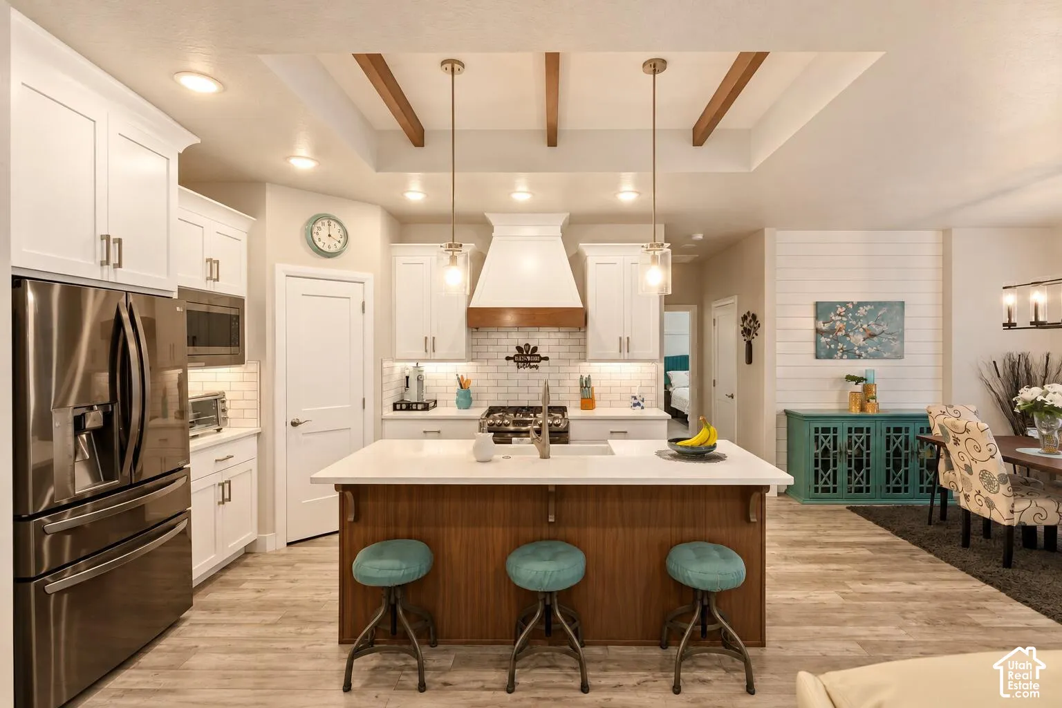 Kitchen featuring a central island with wood cabinetry and quartz countertops, white shaker-style cabinetry, a tile backsplash, stainless steel appliances, and a recessed ceiling with exposed beams