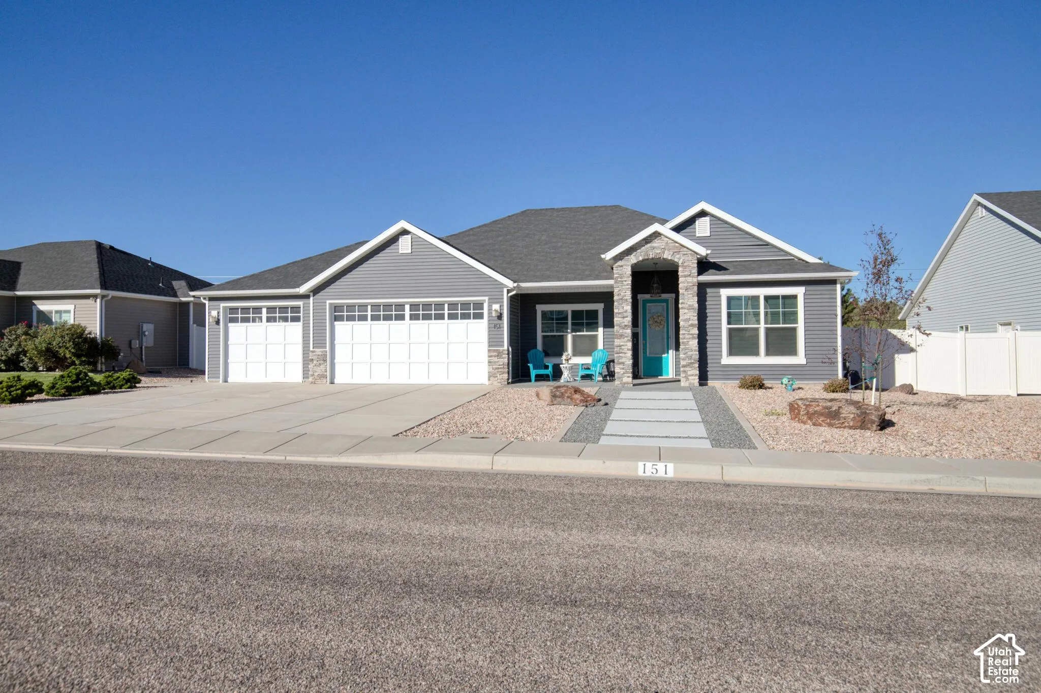 Single-level residence with gray siding, stone masonry accents, a three-car garage, and a paver walkway leading to a covered entryway