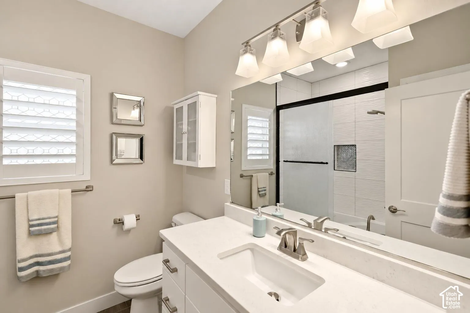 Vanity featuring a white stone countertop, undermount sink, and brushed nickel faucet, paired with a large plate glass mirror, four-light glass vanity fixture, and a white wall-mounted cabinet