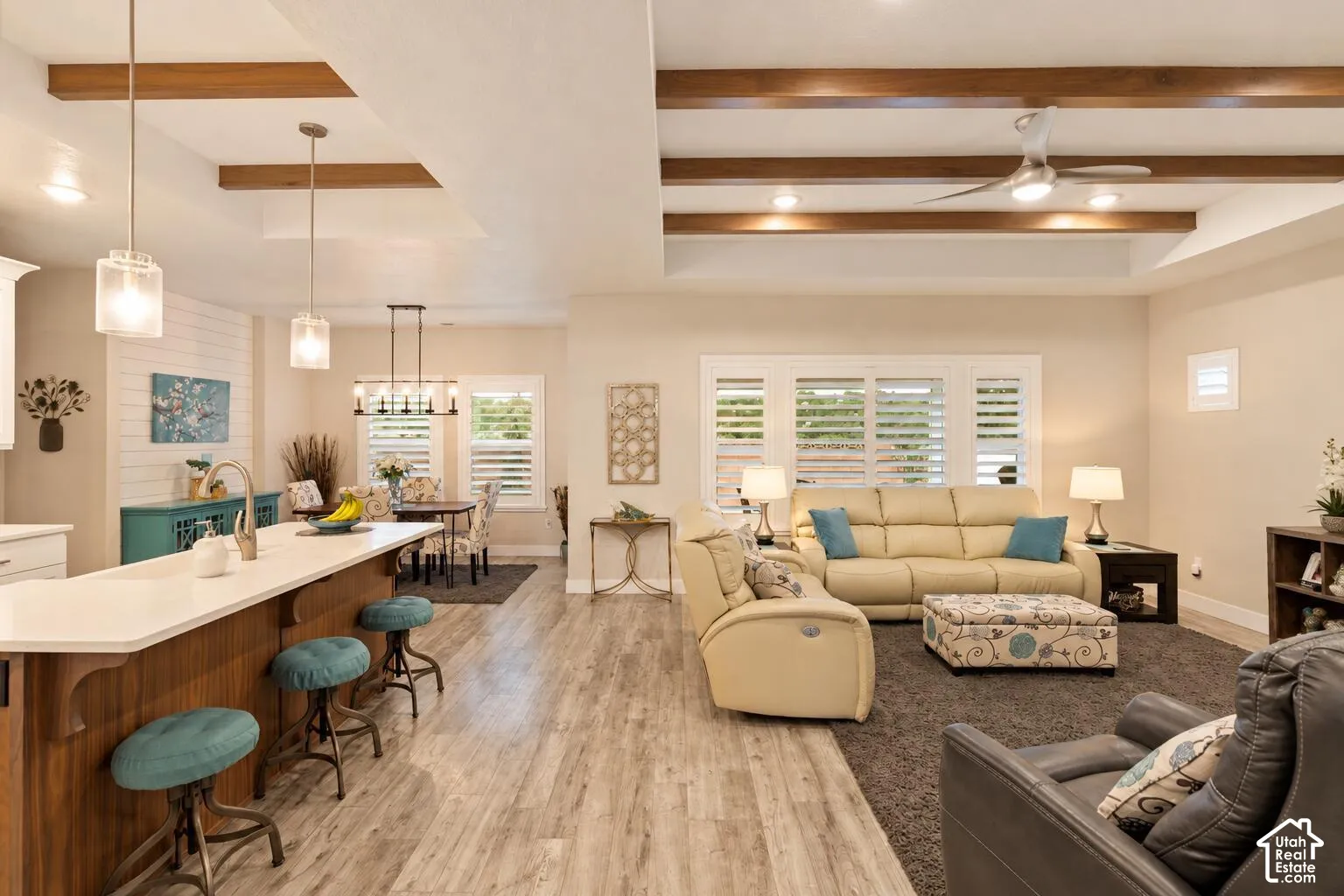 Open-concept living space featuring wood-finish flooring, exposed ceiling beams, recessed lighting, a center island with a quartz countertop, and plantation shutters