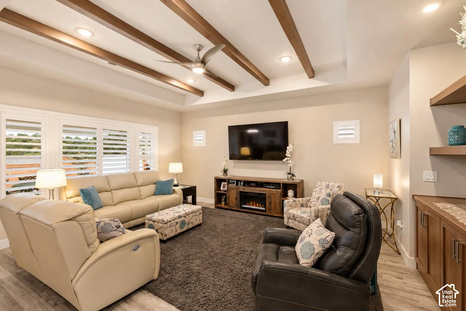 Living area featuring a tray ceiling with exposed wood beams, recessed lighting, wood-finish flooring, plantation shutters, and built-in shelving