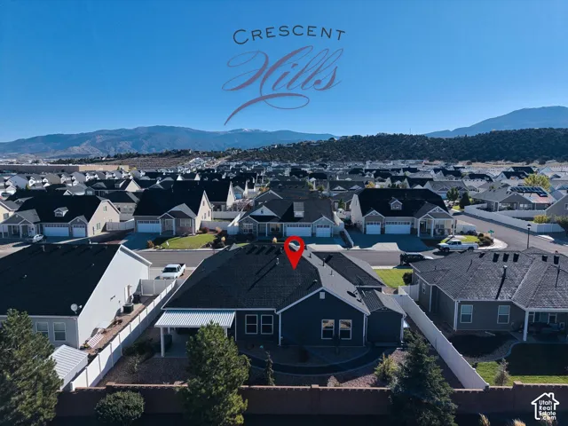 Aerial perspective of a detached residential property featuring a dark-toned exterior, a covered rear patio, a fenced perimeter, and mountain topography in the background