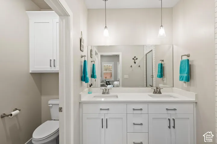 Double vanity featuring white shaker-style cabinetry, quartz countertops, undermount rectangular sinks, dual pendant lighting, and a wall-to-wall vanity mirror
