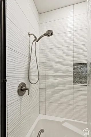 Shower area featuring textured white wall tile, brushed metallic handheld shower head with single-handle mixing valve, and a decorative tile-lined recessed wall niche