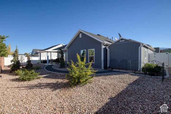 Exterior features include dark-toned horizontal siding, a covered patio, xeriscaped grounds with decorative rock, and perimeter vinyl fencing