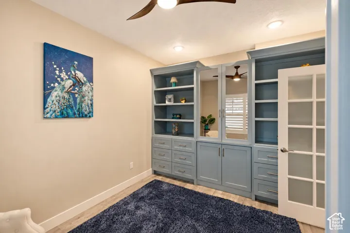 Custom blue built-in cabinetry featuring integrated shelving, lower storage drawers, and mirrored cabinet doors, complemented by a white 10-pane glass panel door, wood-finish flooring, and a modern ceiling fan
