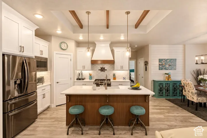 Kitchen featuring a central island with wood cabinetry and quartz countertops, white shaker-style cabinetry, a tile backsplash, stainless steel appliances, and a recessed ceiling with exposed beams