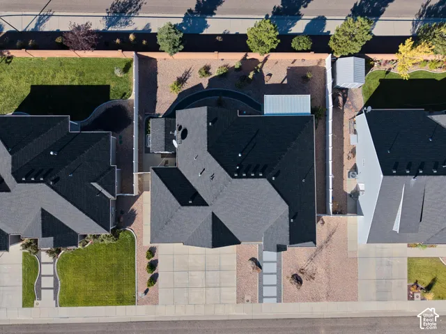 Aerial perspective featuring a multi-pitched asphalt shingle roof, concrete driveway, gravel landscaping, enclosed perimeter fencing, and a detached storage structure