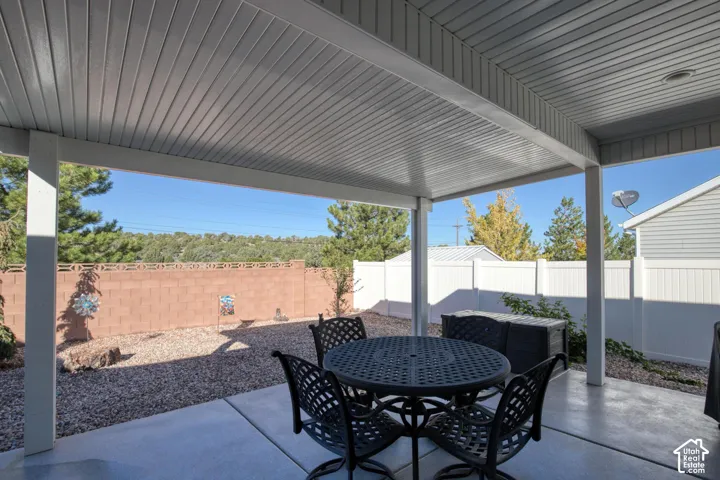 Covered patio with a concrete floor, stone-landscaped backyard, masonry privacy wall, and white vinyl perimeter fencing
