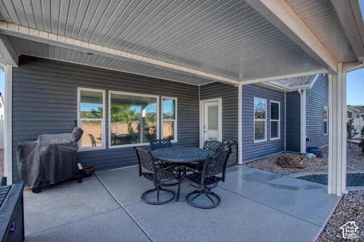 Covered rear patio featuring concrete flooring, dark horizontal siding, and multiple windows