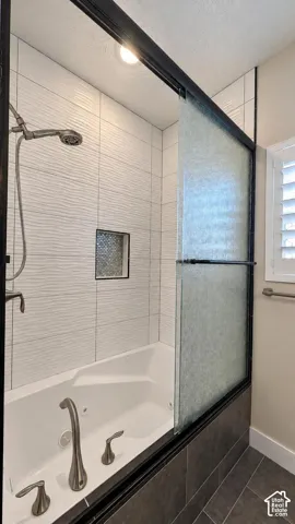 Shower and jetted tub combination featuring textured white wall tile, a recessed niche with decorative mosaic inlay, a sliding glass door with a matte black frame, and brushed nickel hardware