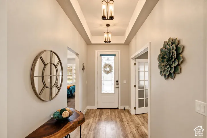 Entryway featuring a coffered ceiling, wood-finish flooring, dual cylinder pendant lighting, and a white door with decorative glass inlay