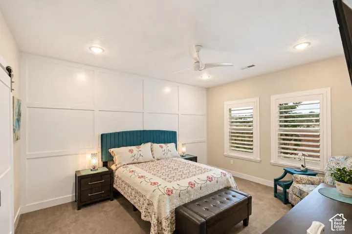 Wall-to-wall carpeting, recessed ceiling lighting, ceiling fan with integrated light fixture, grid-pattern wall molding, and dual windows with plantation shutters