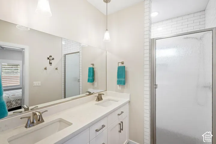 Dual-sink vanity with a solid-surface countertop, full-width wall mirror, pendant lighting, and a glass-enclosed shower with subway tile surround