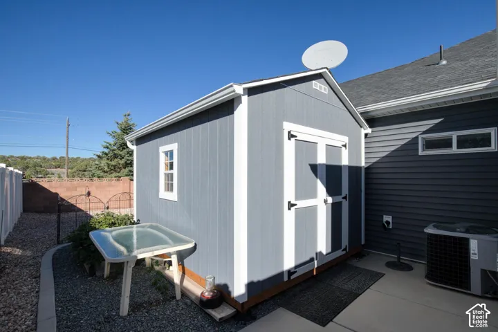 Detached storage structure featuring gray painted siding, white trim, dual entry doors, and a single-pane window