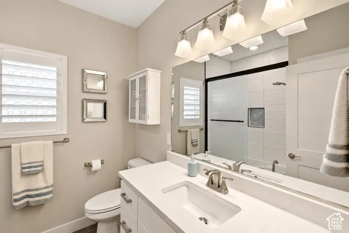 Vanity featuring a white stone countertop, undermount sink, and brushed nickel faucet, paired with a large plate glass mirror, four-light glass vanity fixture, and a white wall-mounted cabinet