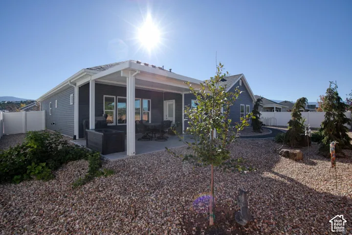 Exterior rear elevation featuring horizontal siding, a covered concrete patio, xeriscaped grounds with decorative rock, and perimeter vinyl fencing